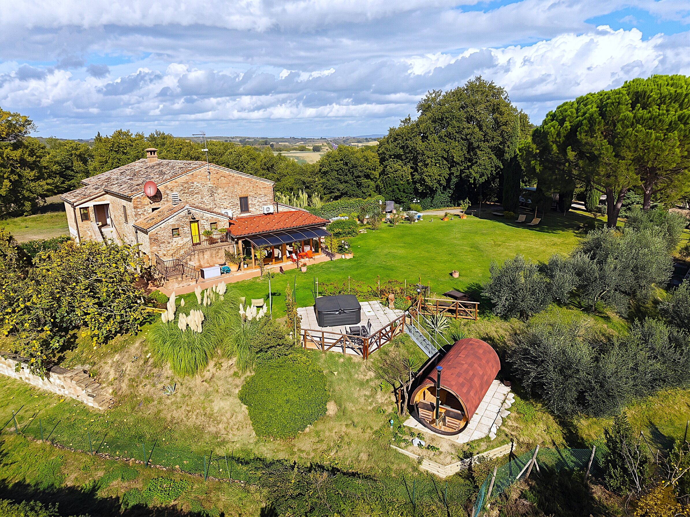 A stone house with a red roof, a covered patio, and a small outdoor kitchen.