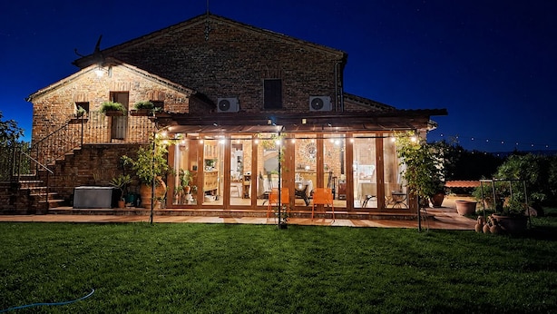 A brick house with a large glass front, outdoor seating, and a well-maintained lawn.