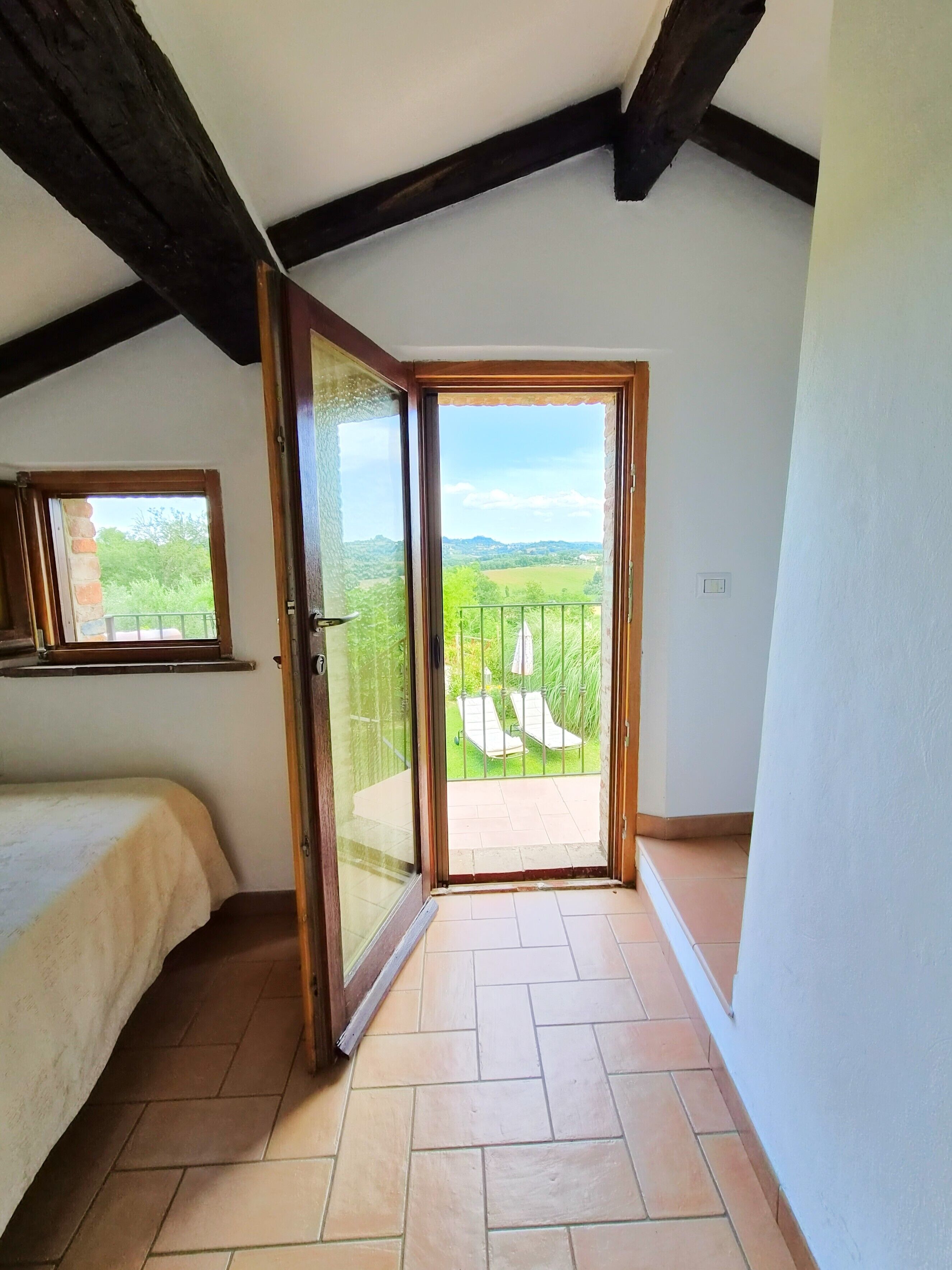 A bedroom with a large sliding glass door leading to a balcony with a view of greenery and hills.