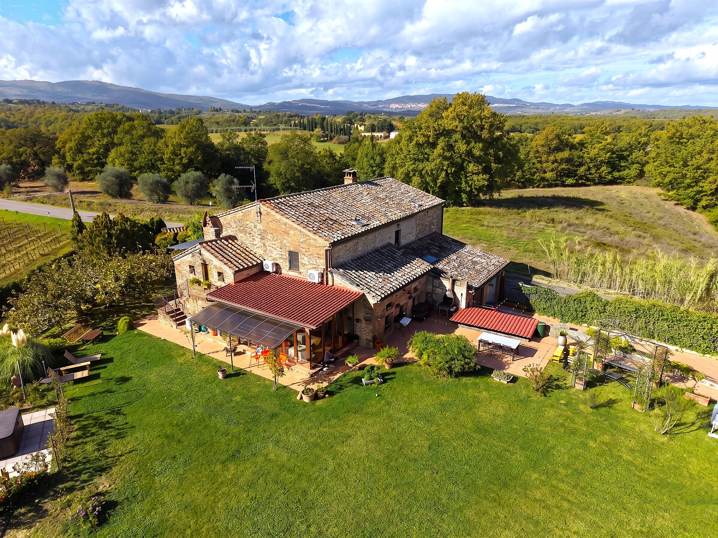 A large stone building with a red-tiled roof, surrounded by lush green fields and trees.
