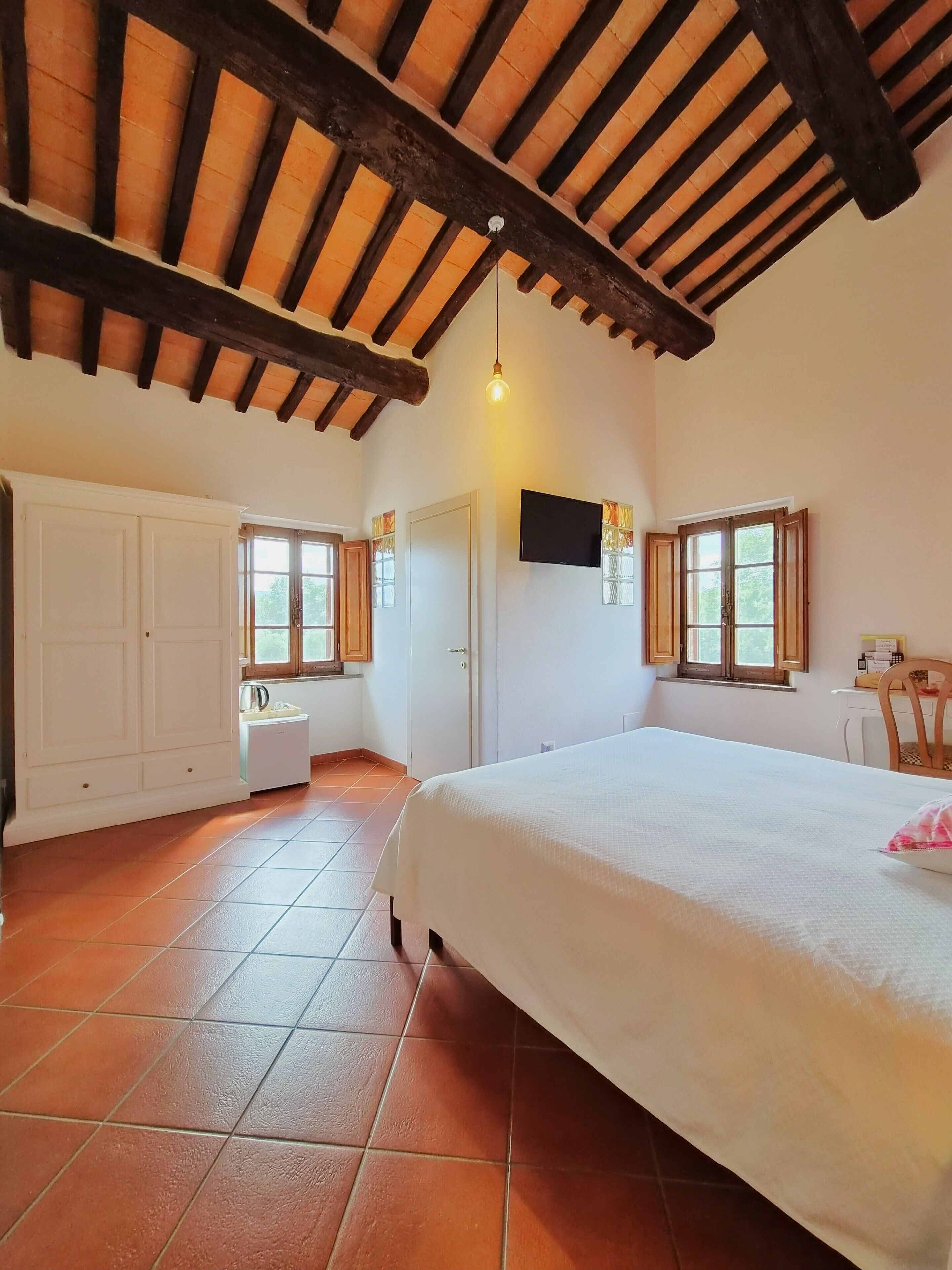 Un dormitorio con cama, televisor, ventana y puerta.