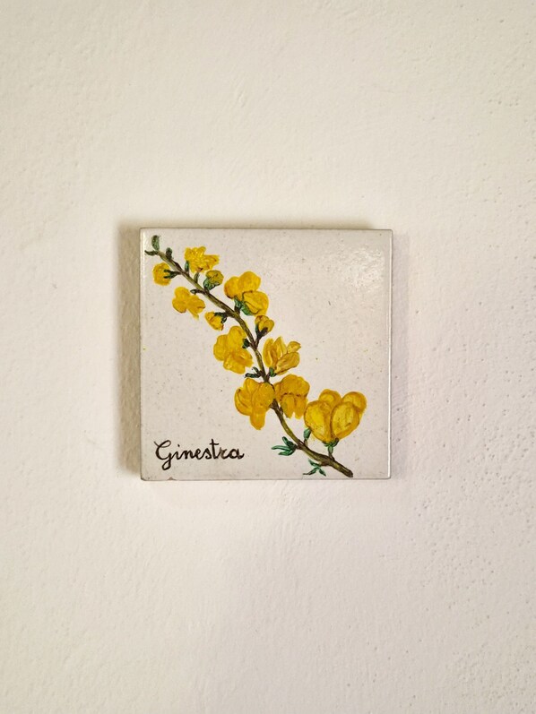 A square tile with a branch of yellow flowers and the word 'Ginestra' on it. - B&B Il Casale di Sandra (Chiusi)