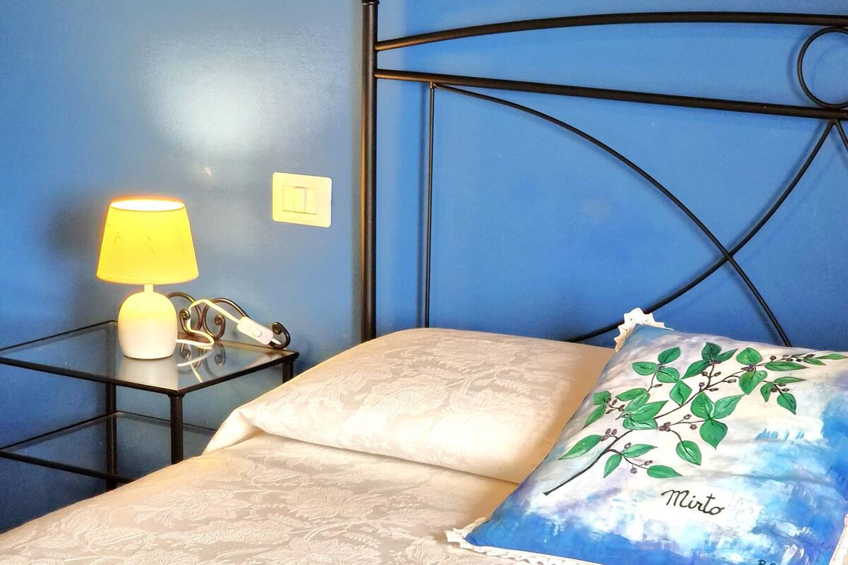 Una cama con una colcha estampada, una lámpara de noche, una mesita de noche con un teléfono y una almohada con motivos naturales.
