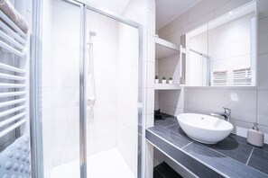 Ein modernes Badezimmer mit Duschkabine aus Glas, einem weißen Waschbecken und einem großen Spiegel.