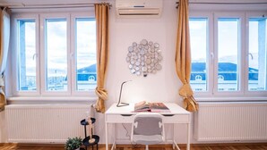Ett rum med ett vitt skrivbord, en stol, ett element, en krukväxt och en väggmonterad luftkonditioneringsanläggning.