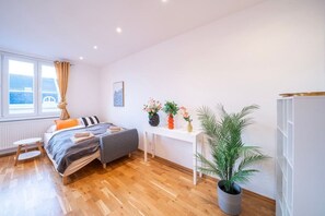 A modern bedroom with a bed, bedside table, potted plant, and a view of the sea through large windows. - 5 min from Hauptbahnhof, 1 Bedroom, AC, Smart TV (Wien)