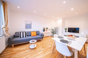 A modern living room with a grey sofa, a dining table with chairs, a flat-screen TV, and a wooden floor. - 5 min from Hauptbahnhof, 1 Bedroom, AC, Smart TV (Wien)