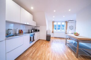 A modern kitchen with white cabinets, a wooden floor, a dining table, and a window with curtains. - 5 min from Hauptbahnhof, 1 Bedroom, AC, Smart TV (Wien)