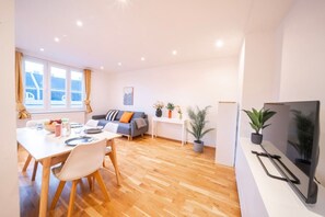 Ein modernes Wohnzimmer mit Essbereich, einer Couch, einem Fernseher und einer Topfpflanze.