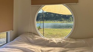 A room with a bed, a circular window, and a view of a lake.