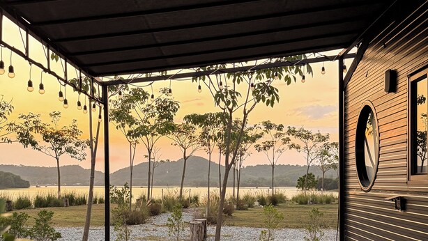 A covered outdoor seating area with a table and chairs, overlooking a body of water and trees.