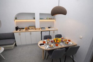 A compact kitchen with a dining area, featuring a breakfast setup with fruits, pastries, and a coffee machine. - Iliana's Getaway - Private Villa with Jacuzzi (Imerovigli)