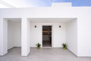A modern building with a white exterior, a central doorway leading to an interior space, and two potted plants on either side of the entrance. - Iliana's Getaway - Private Villa with Jacuzzi (Imerovigli)