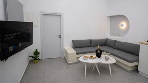 Una sala de estar moderna con televisor de pantalla plana, sofá gris, una mesita redonda y una planta en maceta.