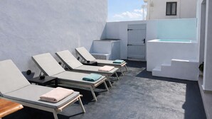 Una terraza en la azotea con sillas de tomar el sol, una mesita y una puerta.
