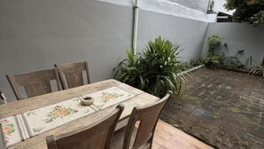 Eine Terrasse mit Tisch und Stühlen, eine graue Wand und ein Gartenbereich.