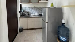 Eine kleine Küche mit Kühlschrank, Wasserspender und einer gefliesten Spritzschutzwand.