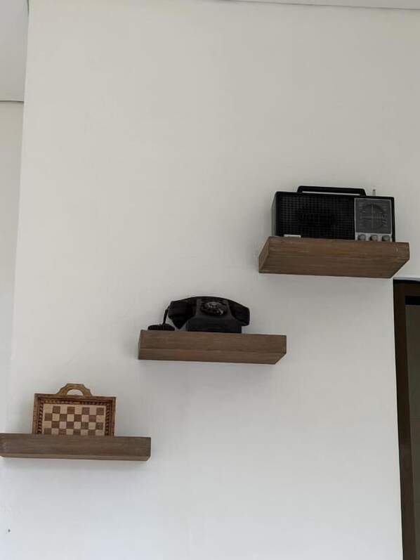A wall with four wooden shelves, each holding different items: a radio, a telephone, and a chessboard. - Pandan de Bali (Kutuh)
