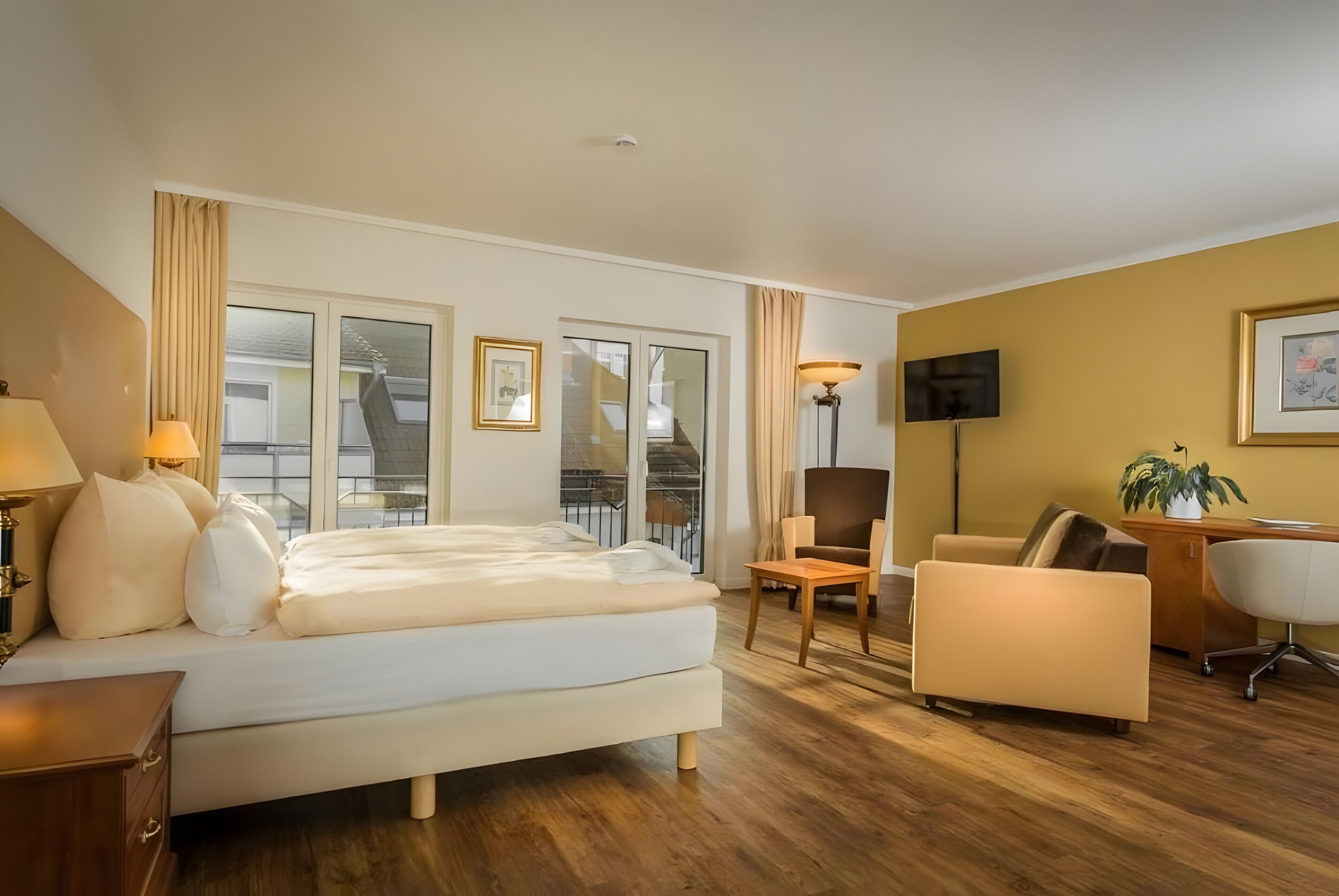 Ein Hotelzimmer mit Bett, Schreibtisch, Stuhl, Fernseher und Balkon.