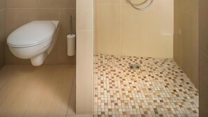 A bathroom with a toilet, a shower with a handheld showerhead, and a tiled floor. - Central Suite ll – Cozy Holiday Home in Greifswald for 2 Guests (Greifswald)