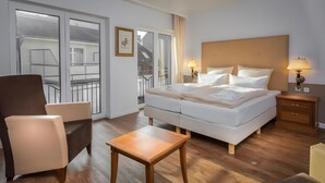 Een hotelkamer met een bed, een stoel, een tafeltje, een nachtkastje en uitzicht op een balkon.