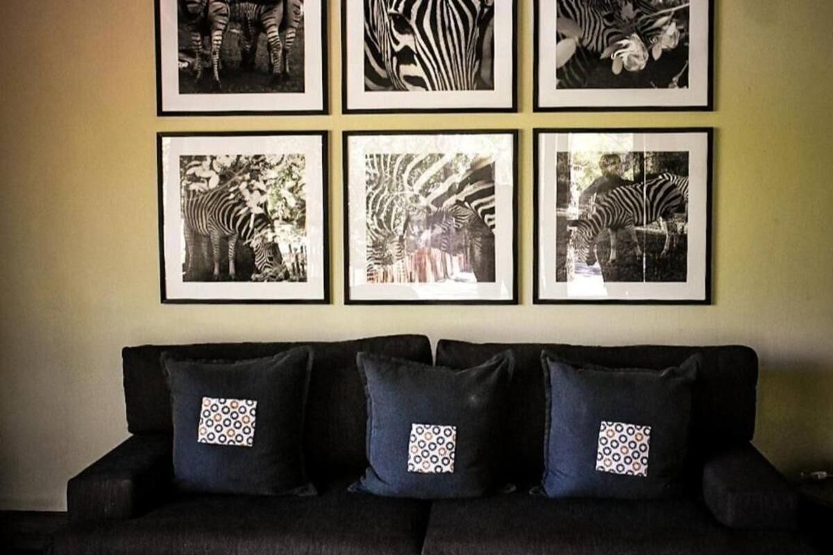 A black sofa with patterned cushions and six framed zebra photographs on the wall.