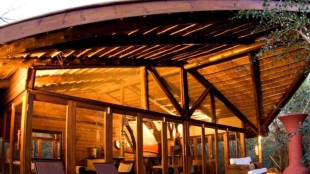 Eine Holzterrasse mit Liegestühlen, ein überdachter Bereich mit Glastüren und ein rustikales Interieur.