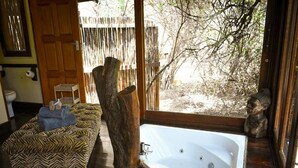 Ein Zimmer mit einer großen Badewanne, einem zebra-gestreiften Sofa, einem Holzbalken und Blick auf Bäume.