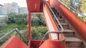 Eine Treppe mit Metallgeländern führt zu einer höheren Ebene, umgeben von Grünpflanzen und Gebäuden im Hintergrund.