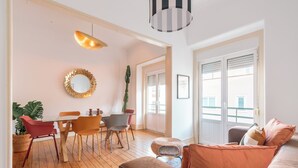 Ein modernes Wohnzimmer mit Holzboden, einem runden Spiegel, einem Esstisch mit Stühlen, einer Couch und einer hängenden Leuchte.