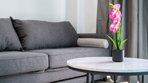 Een moderne woonkamer met een grijze bank, een ronde salontafel met een orchidee in pot, en een minimalistische inrichting.