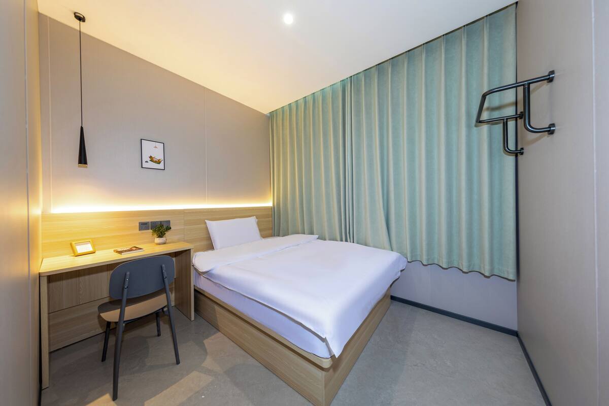Habitación de hotel con cama, escritorio, silla y ventana con cortinas.