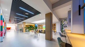 Un espacio interior amplio con un diseño de techo moderno, un área de estar central con mesas y sillas, y una estantería llena de libros.