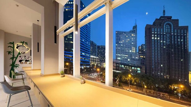 Habitación moderna con un amplio ventanal que ofrece vistas a un paisaje urbano al atardecer.