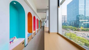 Un pasillo con nichos coloridos, vistas de un paisaje urbano a través de amplias ventanas y fachada de un edificio moderno.