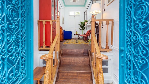 A staircase with ornate railings leading to a room with a red door and a chandelier.