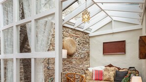 A conservatory with a stone wall, wicker furniture, and a hanging light fixture.