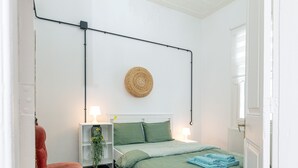 A bedroom with a bed, bedside lamps, a wall-mounted light fixture, a woven wall hanging, and a radiator.