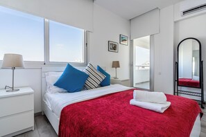 Ein Schlafzimmer mit einem Bett, einer roten Decke, einem weißen Handtuch, einem Nachttisch, einer Lampe, einem Fenster und einem Spiegel.