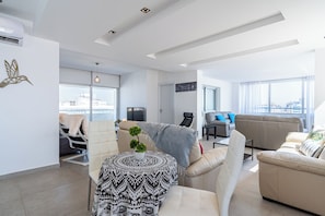 Ein modernes Wohnzimmer mit einer Couch, Sesseln, einem Couchtisch und einem Fernseher.