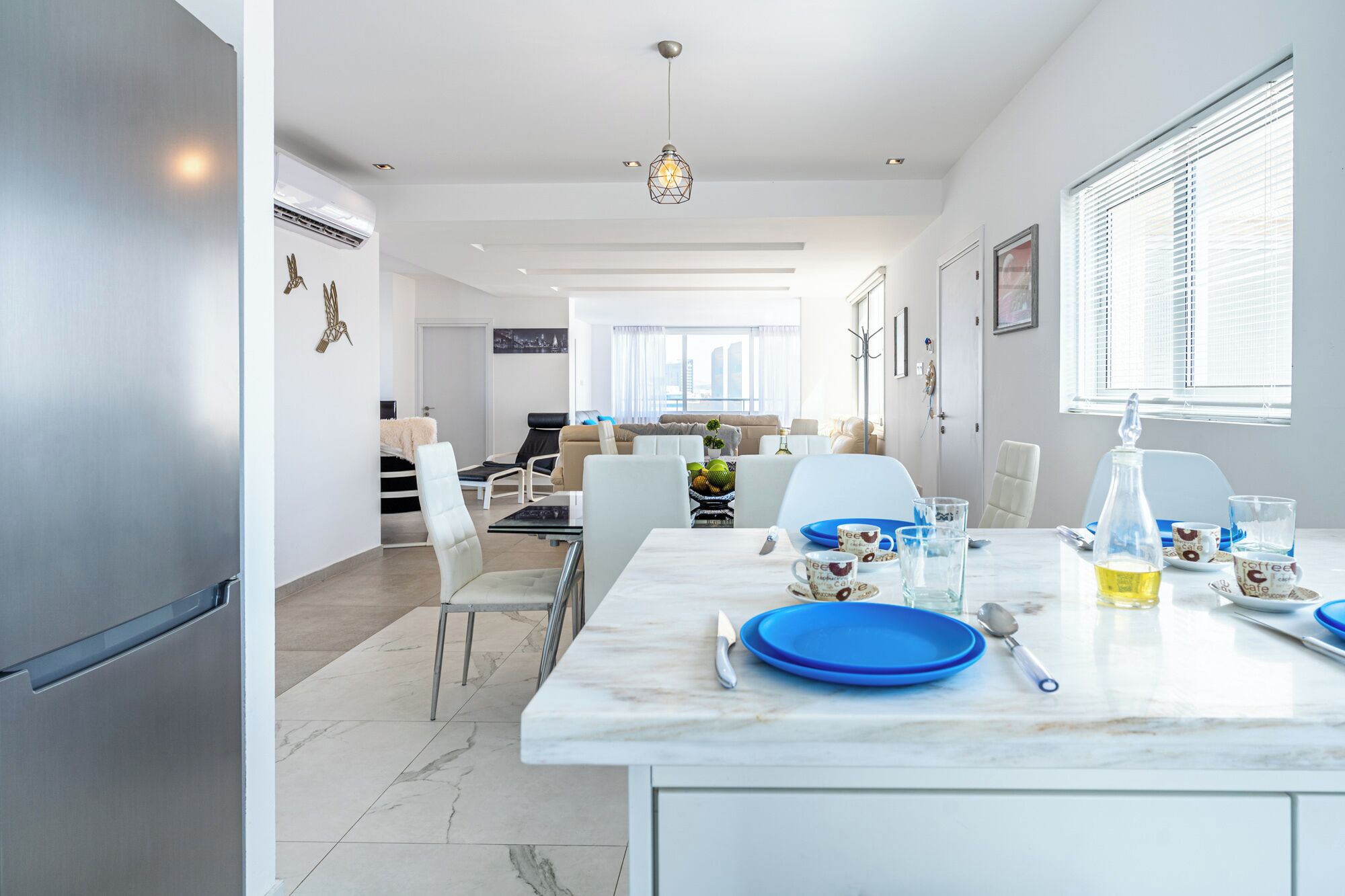 Cozinha moderna com bancada de mármore, área de jantar com cadeiras e vista para a cidade.