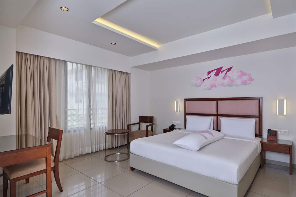 A hotel room with a large bed, a desk, a chair, a small table, and a wall-mounted phone.