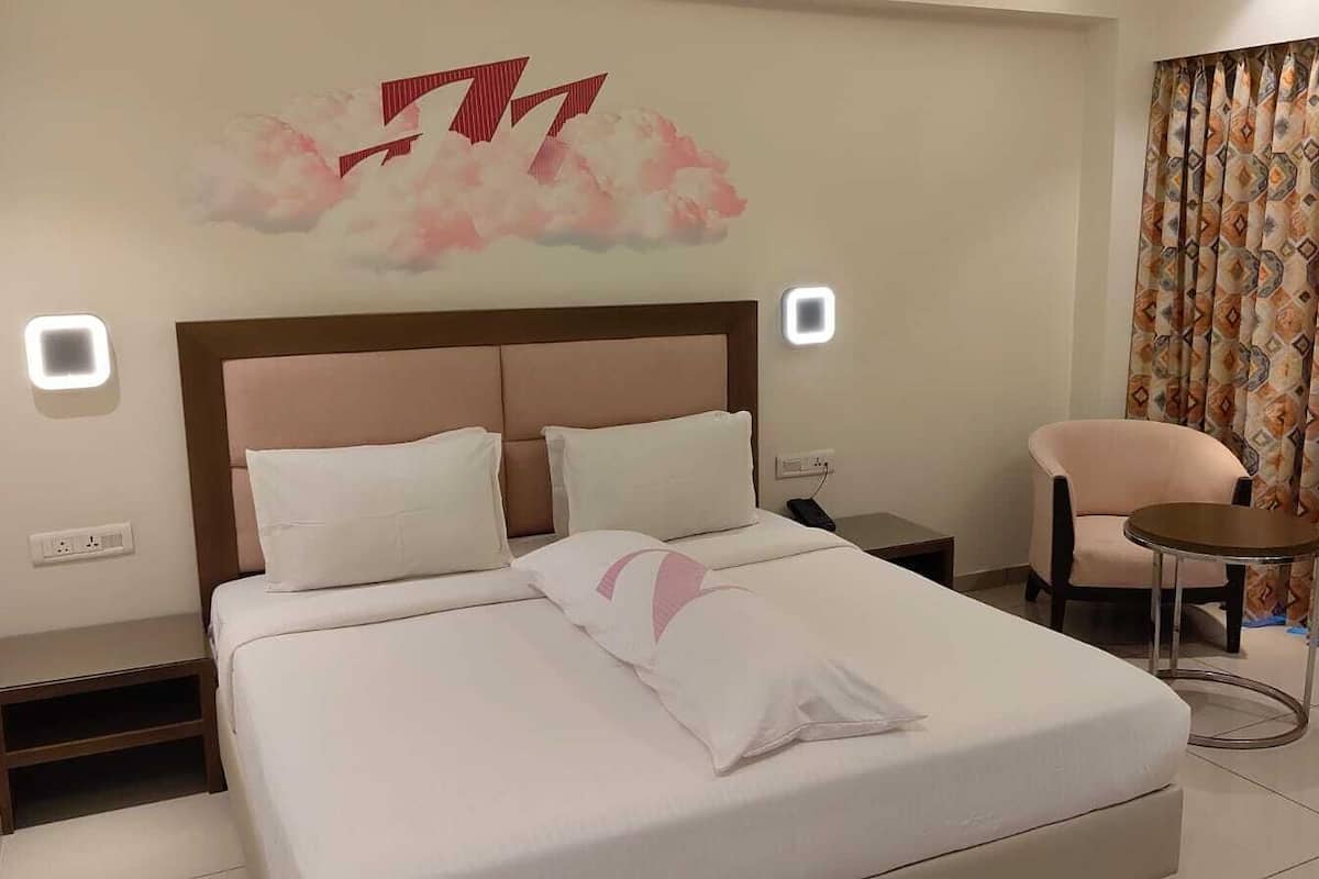A hotel room with a bed, a chair, a nightstand, and a wall-mounted light fixture.
