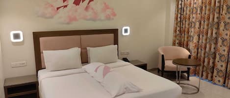 A hotel room with a bed, a chair, a nightstand, and a wall-mounted light fixture.