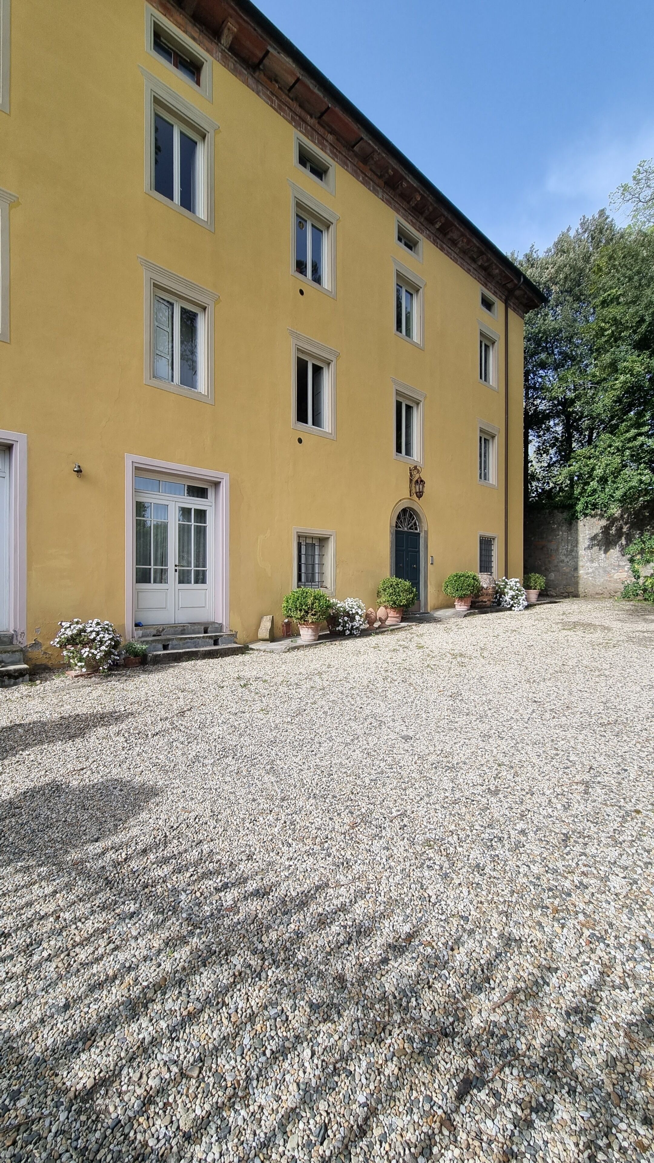 A yellow building with multiple windows and a door, surrounded by gravel and potted plants.