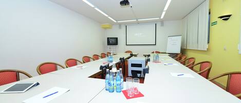 A conference room with a long table, chairs, a projector, a screen, and a whiteboard.