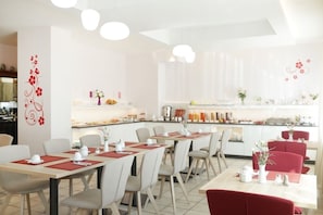 A modern dining area with tables set for service, a kitchen in the background, and decorative wall art. - Hotel am Buchwald (Esslingen)