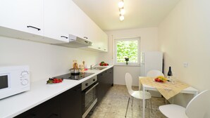 A compact kitchen with a microwave, stove, and sink, a dining table with chairs, and a window with a view of greenery. - Hotel am Buchwald (Esslingen)