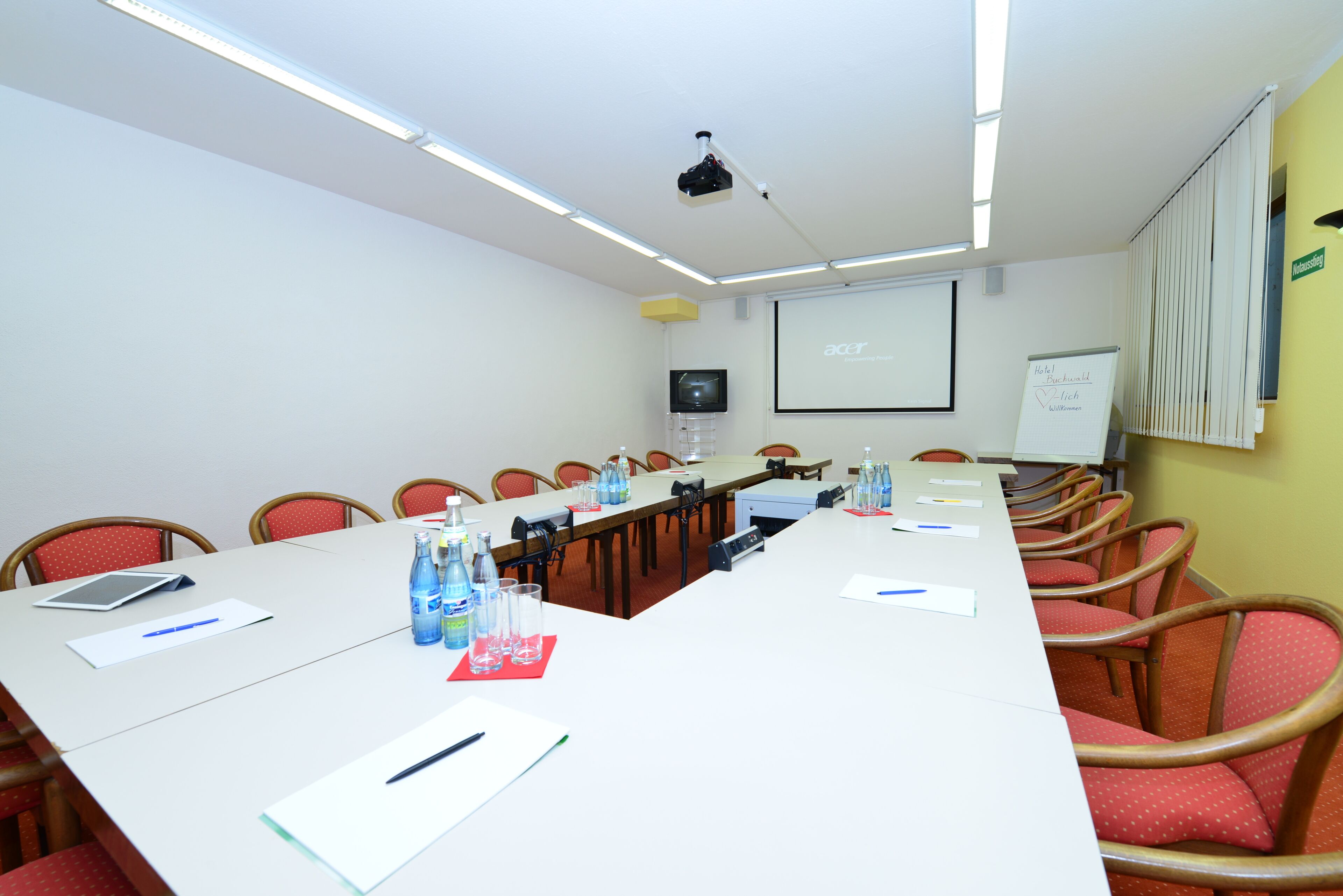 Sala de conferência com uma mesa comprida, cadeiras, um projetor, uma lousa branca e uma tela exibindo a marca Acer.