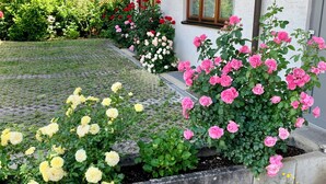 A garden with various flowering plants, a paved walkway, and a building with windows. - Hotel am Buchwald (Esslingen)